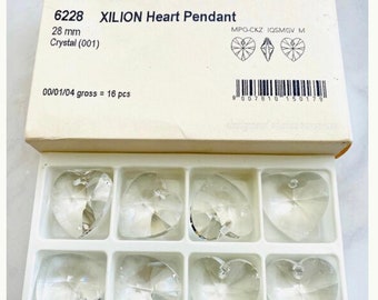 May include: A box of 16 clear crystal XILION Heart Pendants, each measuring 28 mm. The box is white with black text and a barcode. The pendants are arranged in a grid pattern.
