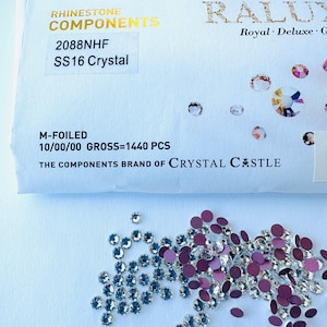 May include: A close-up of a packet containing 1440 clear rhinestones in size SS16. The packet is labelled "Rhinestone Components" and "2088NHF". The rhinestones are scattered on a white surface.
