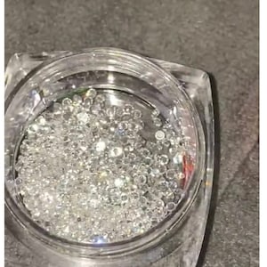 Puede incluir: Un frasco de vidrio transparente lleno de pequeños diamantes de imitación plateados iridiscentes.