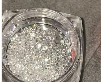 May include: A clear glass jar filled with small, iridescent, silver-colored rhinestones.