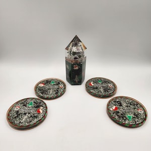 May include: A Christmas-themed gift set featuring a decorative prism with a Santa Claus figure inside, and four oval coasters. The coasters have a green and red border, with a Christmas tree, Santa hat, and the words "Merry Christmas".