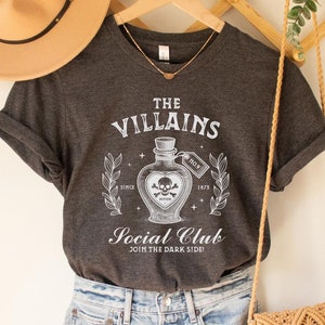 May include: Dark grey heather V-neck t-shirt with a white graphic of a potion bottle with a skull and crossbones. The text "The Villains Social Club Join the Dark Side" is printed on the shirt.