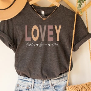 May include: Dark grey heather t-shirt with the word "LOVEY" printed in pink, orange, and brown. The text "Abbley Briana Adam" is printed below the word "LOVEY" in a smaller font.