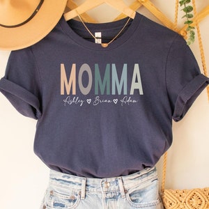 May include: Navy blue t-shirt with the word "MOMMA" in rainbow colors and the names "Ashley", "Brian", and "Aidan" written below.