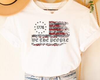 May include: White t-shirt with a distressed American flag design and the text "1776 We the People".