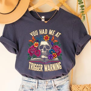 May include: Navy blue t-shirt with a skull and flowers graphic and the text "You had me at trigger warning".