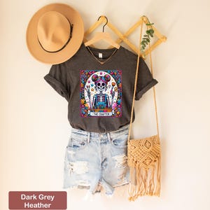 May include: Dark grey heather V-neck t-shirt featuring a colourful illustration of a skeleton with flowers and the text "The Crafter".