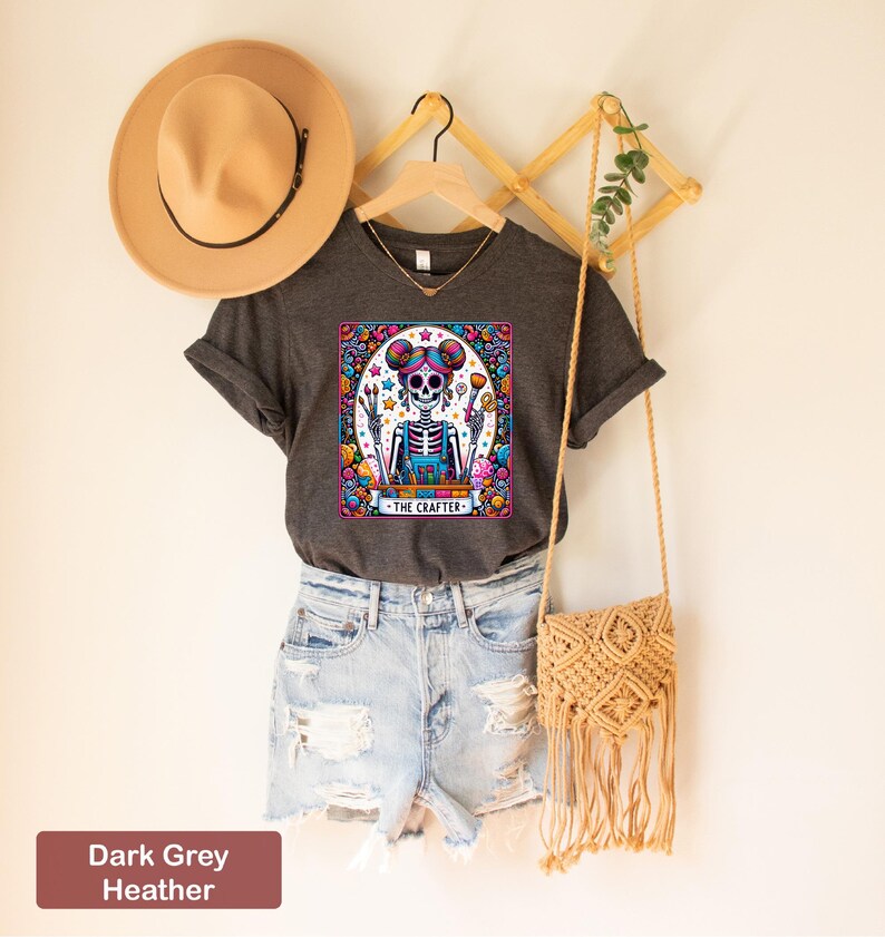 May include: Dark grey heather V-neck t-shirt featuring a colourful illustration of a skeleton with flowers and the text "The Crafter".