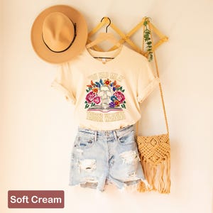 Puede incluir: Una camiseta de color crema con un gr&aacute;fico de calavera y flores y el texto "You had me at trigger warning".