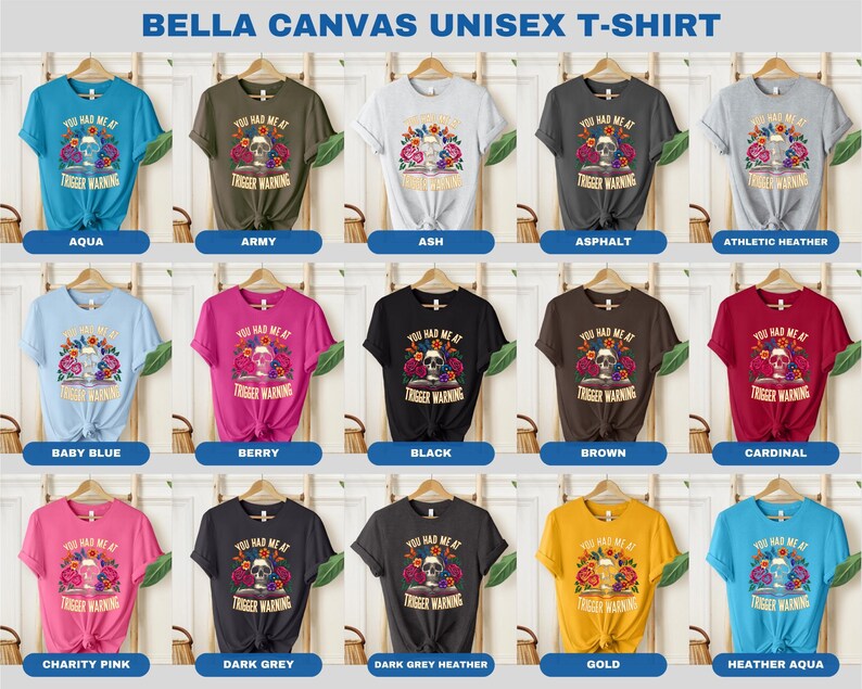Puede incluir: Una maqueta de una camiseta unisex en 15 colores diferentes con una calavera con flores y el texto "You Had Me At Trigger Warning".