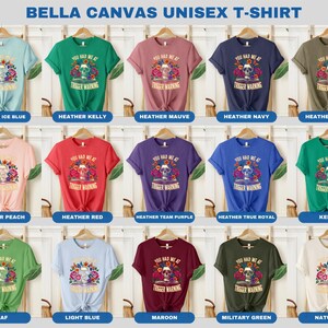 Puede incluir: Una camiseta unisex Bella Canvas con una calavera con flores y el texto "You Had Me At Trigger Warning". La camiseta est&aacute; disponible en 15 colores diferentes, incluyendo azul hielo jaspeado, kelly jaspeado, malva jaspeado, azul marino jaspeado, oliva jaspeado, melocot&oacute;n jaspeado, rojo jaspeado, morado jaspeado, azul real jaspeado, kelly, hoja, azul claro, granate, verde militar y natural.