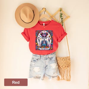 May include: Red t-shirt featuring a colourful illustration of a skeleton holding paintbrushes and a palette. The text "The Crafter" is below the illustration.