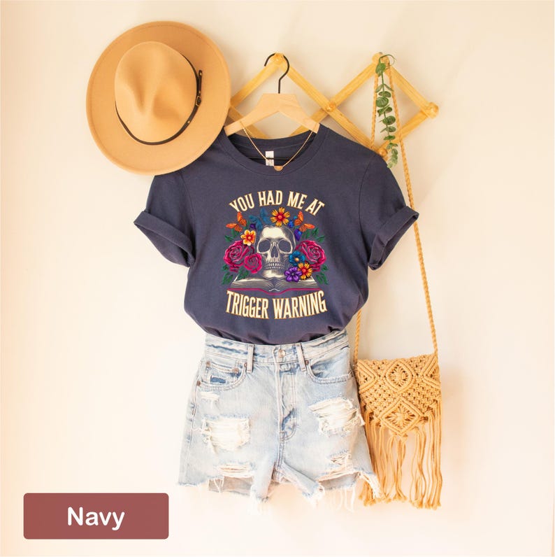 Puede incluir: Camiseta azul marino con un gr&aacute;fico de calavera y flores y el texto "You had me at trigger warning".