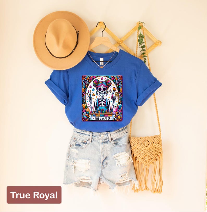 May include: A blue t-shirt featuring a colourful illustration of a skeleton holding paintbrushes and a palette. The text "The Crafter" is below the image.