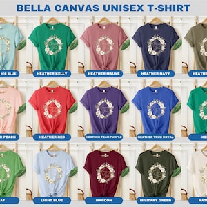 May include: A Bella Canvas unisex t-shirt featuring a floral wreath design with the text "Forever Young" in gold lettering. The shirt is available in 15 different colours, including Heather Ice Blue, Heather Kelly, Heather Mauve, Heather Navy, Heather Olive, Heather Peach, Heather Red, Heather Team Purple, Heather True Royal, Kelly, Leaf, Light Blue, Maroon, Military Green, and Natural.