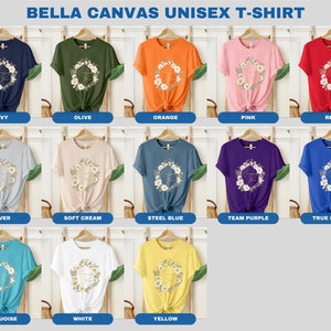 May include: A Bella Canvas unisex t-shirt featuring a floral wreath with the text "Thank You" in gold lettering. The shirt is available in 12 colours: navy, olive, orange, pink, red, silver, soft cream, steel blue, team purple, true royal, turquoise, white, and yellow.