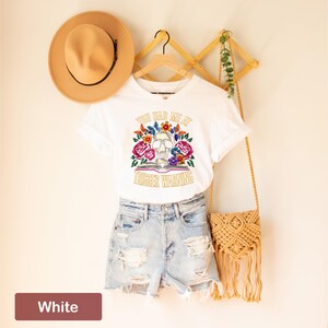 Puede incluir: Camiseta blanca con un gr&aacute;fico de calavera y flores y el texto "You had me at trigger warning".