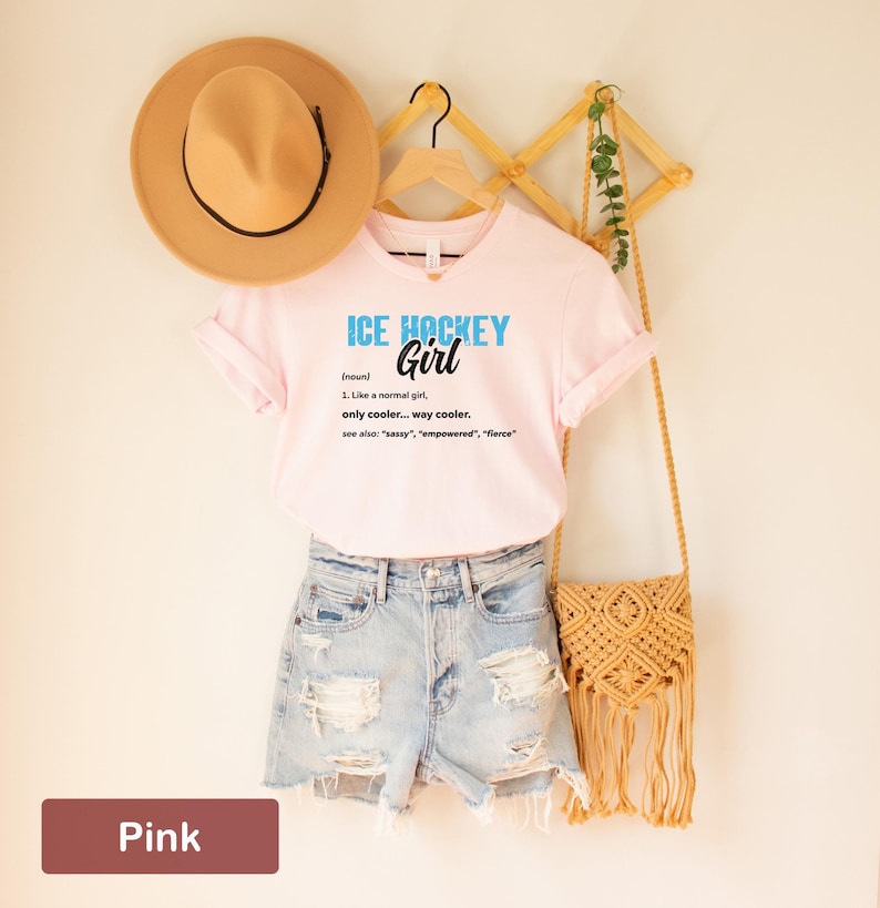 Op de afbeelding: Roze T-shirt met de tekst "ICE HOCKEY Girl (zelfstandig naamwoord) 1. Net als een normaal meisje, alleen cooler... veel cooler. zie ook: "sassy", "empowered", "fierce" "