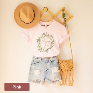 May include: Pink t-shirt featuring a floral wreath design with the text "Amazing Grace" in gold lettering.