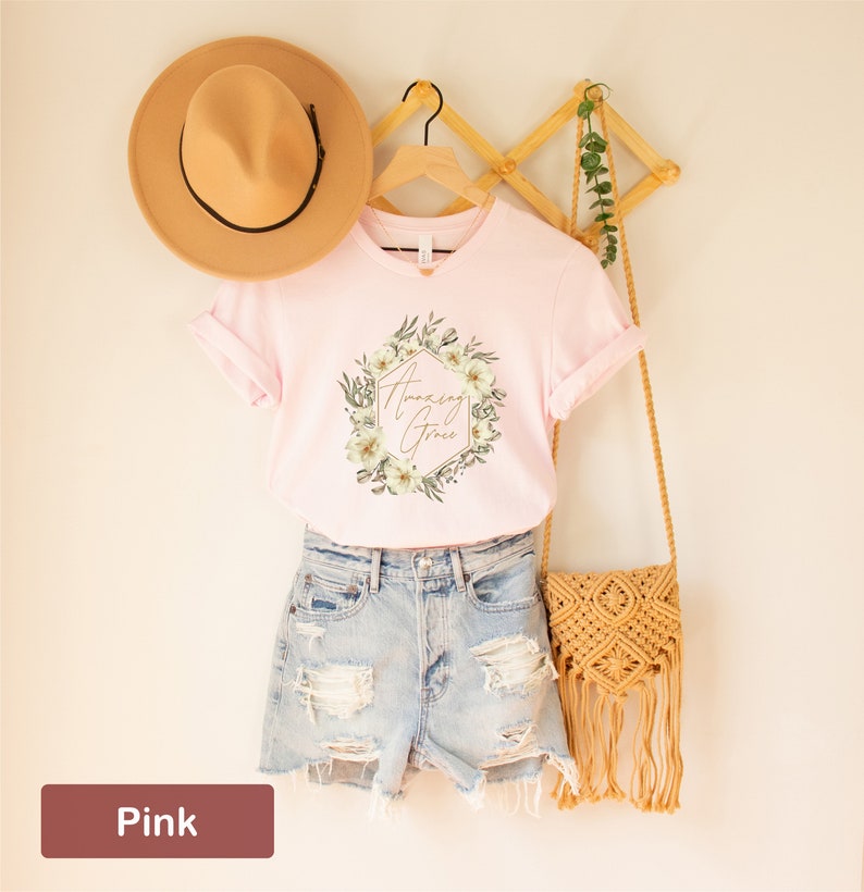 May include: Pink t-shirt featuring a floral wreath design with the text "Amazing Grace" in gold lettering.