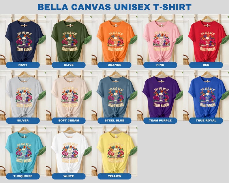 Puede incluir: Una camiseta unisex Bella Canvas con una calavera con flores y el texto "You had me at trigger warning". La camiseta est&aacute; disponible en 12 colores: azul marino, oliva, naranja, rosa, rojo, plata, crema suave, azul acero, morado equipo, azul real, turquesa, blanco y amarillo.