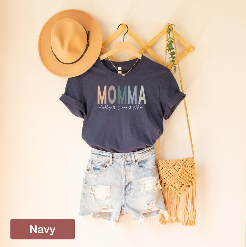May include: Navy blue t-shirt with the word "MOMMA" in rainbow colors and the names "Ashley", "Brian", and "Aidan" written below.