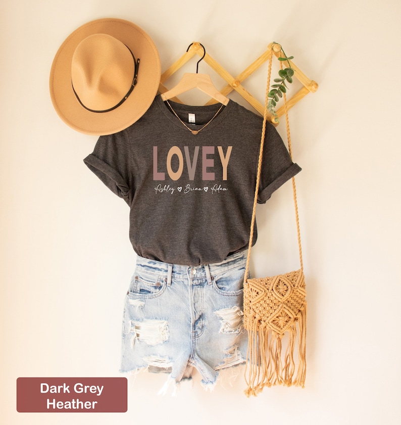 May include: Dark grey heather t-shirt with the word "LOVEY" printed in pink, orange, and brown. The text "Abbley Briana Adam" is printed below the word "LOVEY" in a smaller font.
