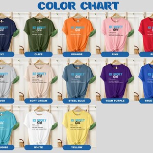Op de afbeelding: Kleurenkaart met 12 verschillende T-shirt kleuren. Elk T-shirt heeft een grafische print met de woorden "ICE HOCKEY Girl" met een definitie van de term. De kleuren zijn: Navy, Olijf, Oranje, Roze, Rood, Zilver, Zachte Cr&egrave;me, Staalblauw, Team Paars, Koninklijk Blauw, Turquoise, Wit en Geel.