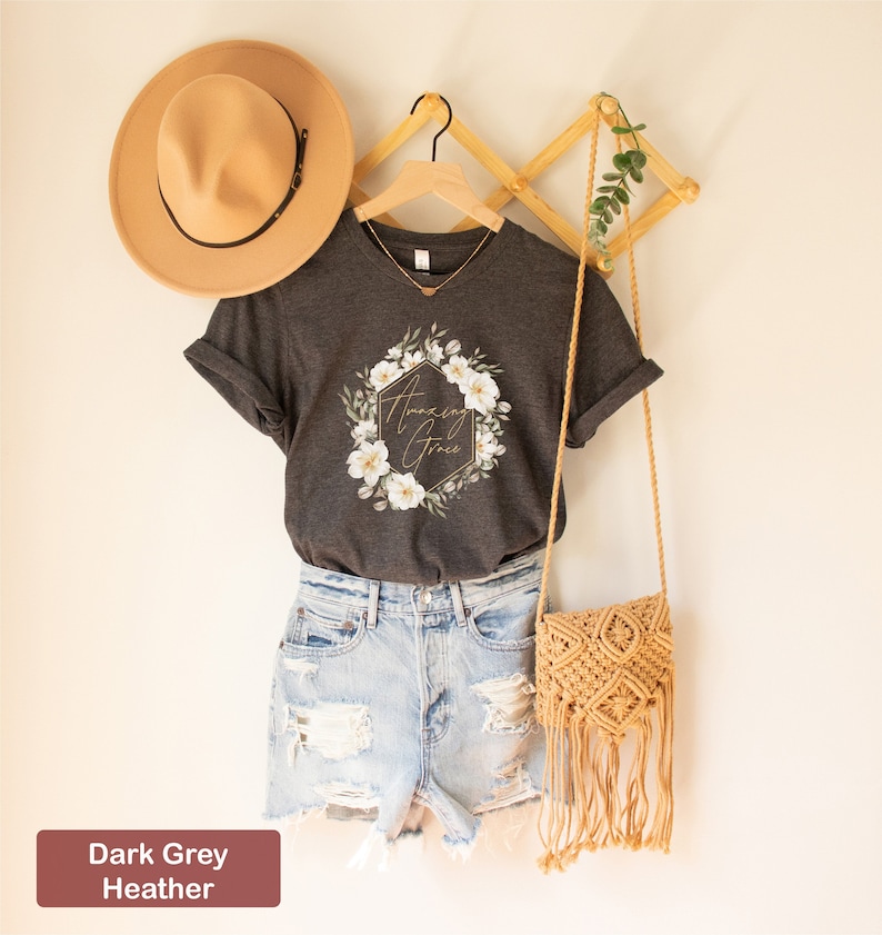 May include: Dark grey heather t-shirt with a floral wreath design and the text "Amazing Grace" in gold lettering.
