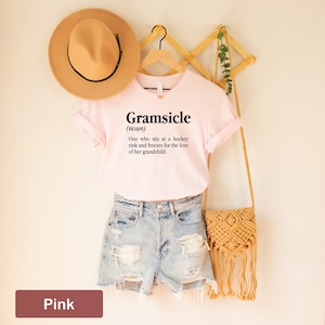May include: Pink t-shirt with the text "Gramsicle (noun) One who sits at a hockey rink and freezes for the love of her grandchild."