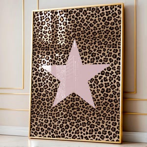 May include: A framed art print with a leopard print pattern and a large, pale pink star. The frame is gold-coloured. The artwork is a decorative piece for a wall.