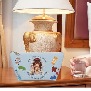 May include: Light blue makeup bag with a cartoon illustration of a woman with a headache and the text "At the effects of a hangover, I miss the fun of going out".