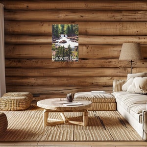 May include: A framed landscape art print depicting a waterfall and river scene with green trees and the text "Beaver Bay". The artwork hangs on a wooden wall in a living room setting with a round wooden coffee table and a beige sofa.