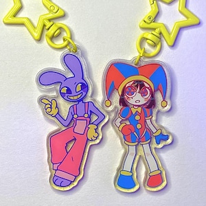 May include: Two acrylic keyrings featuring cartoon characters. One is a purple rabbit in pink dungarees, the other a jester in a red, blue, and yellow outfit. Both have yellow star-shaped clasps.