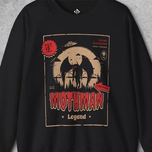 May include: A black sweatshirt featuring a graphic print of the Mothman with red eyes, a large moon, a UFO, and the text "DEC 15 1967", "POINT PLEASANT WEST VIRGINIA", "SILVER BRIDGE", "CRYPTID", "MOTHMAN", and "Legend" in red and cream colours.