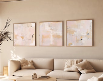 May include: A light beige sectional sofa with three throw pillows in a living room setting. Three abstract paintings in light pink, beige, and white tones hang on the wall above the sofa. A wooden coffee table sits in front of the sofa.