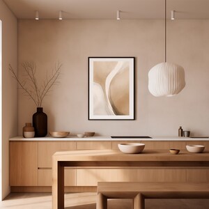 May include: A modern kitchen with light wood cabinetry and a matching island. A framed abstract art piece hangs on the wall. A white, textured pendant light hangs above the island. Decorative bowls and a vase with branches add to the decor.