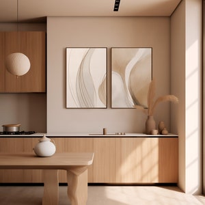 May include: A modern kitchen with light wood cabinetry and a matching wooden table. Two framed abstract art pieces hang on the wall. A white teapot sits on the table. A decorative light fixture hangs from the ceiling.