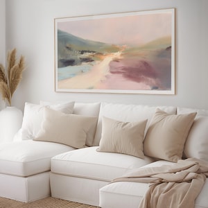 May include: Abstract landscape painting in a light wood frame. The artwork features a blend of colours, including pink, blue, and beige, creating a soft, dreamy aesthetic. The painting hangs above a white sectional sofa with beige cushions.