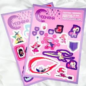 Pode incluir: Duas folhas de adesivos com fundo rosa e borda roxa. Os adesivos apresentam arte pixelizada de personagens, corações e um escudo. O texto "MOONANA" e "sticker sheet" são visíveis. O endereço do site também é visível.
