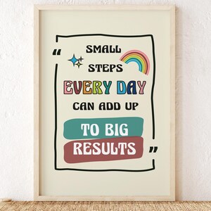 Puede incluir: Una impresión enmarcada con el texto "Small Steps Every Day Can Add Up To Big Results". La impresión tiene un fondo beige claro con texto colorido y un arcoíris. Se muestra en un banco tejido con dos candelabros de vidrio decorativos.