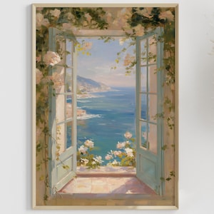 Puede incluir: Una impresión artística enmarcada representa una ventana abierta con vistas a una escena costera. La ventana está enmarcada con molduras azul claro y adornada con rosas trepadoras. La vista incluye un mar azul, cielo y costa distante. Hay tallos de hierba de la Pampa a la derecha.