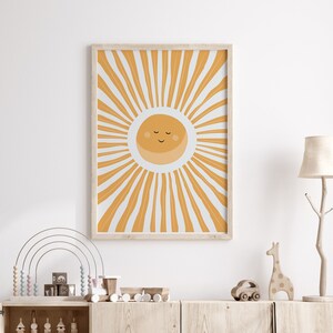 Puede incluir: Una impresión enmarcada de un sol amarillo con una cara sonriente y los ojos cerrados. El sol está rodeado de rayos amarillos y blancos.