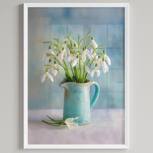 Puede incluir: Impresión enmarcada que presenta un ramo de flores de campanillas blancas en una jarra de cerámica turquesa. La jarra tiene un asa y un pico. El fondo es azul suave con un patrón similar a una ventana.