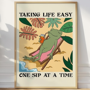 Puede incluir: Una impresión artística enmarcada que presenta una rana de dibujos animados relajándose en una tumbona, bebiendo una bebida. La obra de arte tiene un estilo retro con el texto "TAKING LIFE EASY" y "ONE SIP AT A TIME". El fondo incluye hojas tropicales y una playa arenosa.