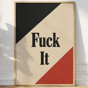Puede incluir: Una lámina de arte mural rectangular en un marco de madera clara con un diseño geométrico que presenta un triángulo negro en la parte superior izquierda y un triángulo rojo en la parte inferior derecha sobre un fondo crema. El texto "Fuck It" está impreso en fuente serif negra.