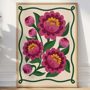 Puede incluir: Una impresión artística enmarcada con un diseño floral. La impresión presenta flores magenta con centros amarillos y hojas verdes, sobre un fondo crema con un borde verde, todo dentro de un marco dorado. La obra de arte evoca un estilo vintage o folk.