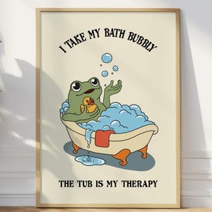 Puede incluir: Un póster enmarcado con una rana de dibujos animados en una bañera llena de burbujas. La rana sostiene un patito de goma. El texto dice: "I take my bath bubbly, the tub is my therapy."