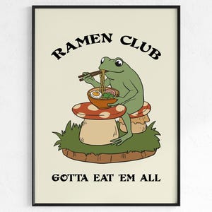 Puede incluir: Impresión artística enmarcada con una ilustración de una rana verde comiendo ramen. La rana está sentada en una seta y sostiene palillos chinos. El texto dice "RAMEN CLUB" y "GOTTA EAT 'EM ALL".