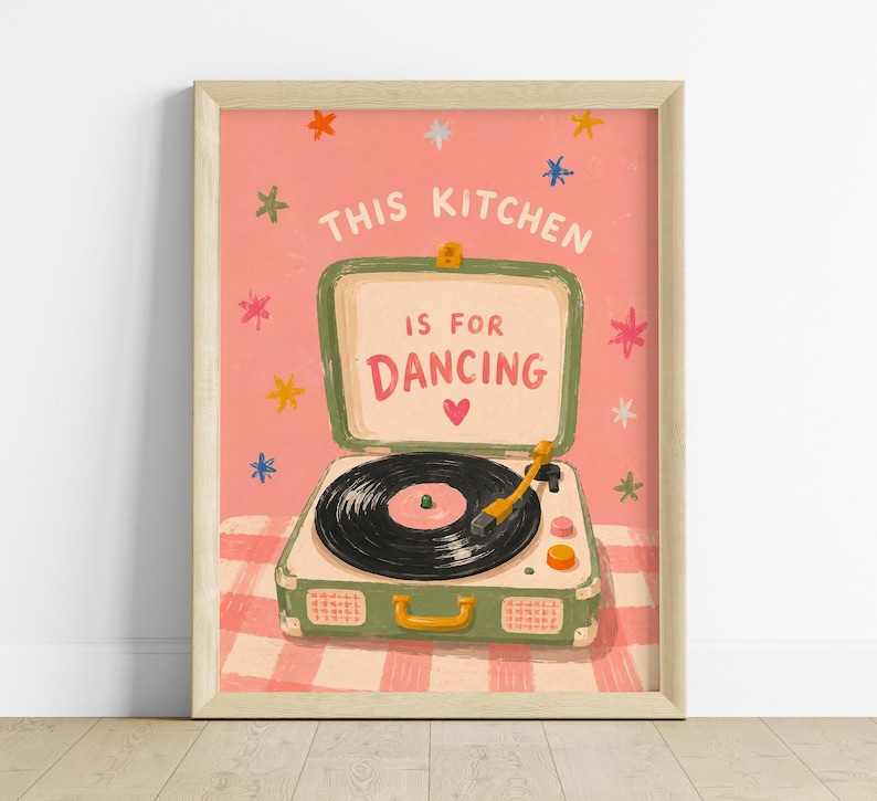 May include: A framed art print featuring a vintage-style record player with the text "THIS KITCHEN IS FOR DANCING." The artwork has a pink background with colorful star accents and a checkered pattern at the bottom.